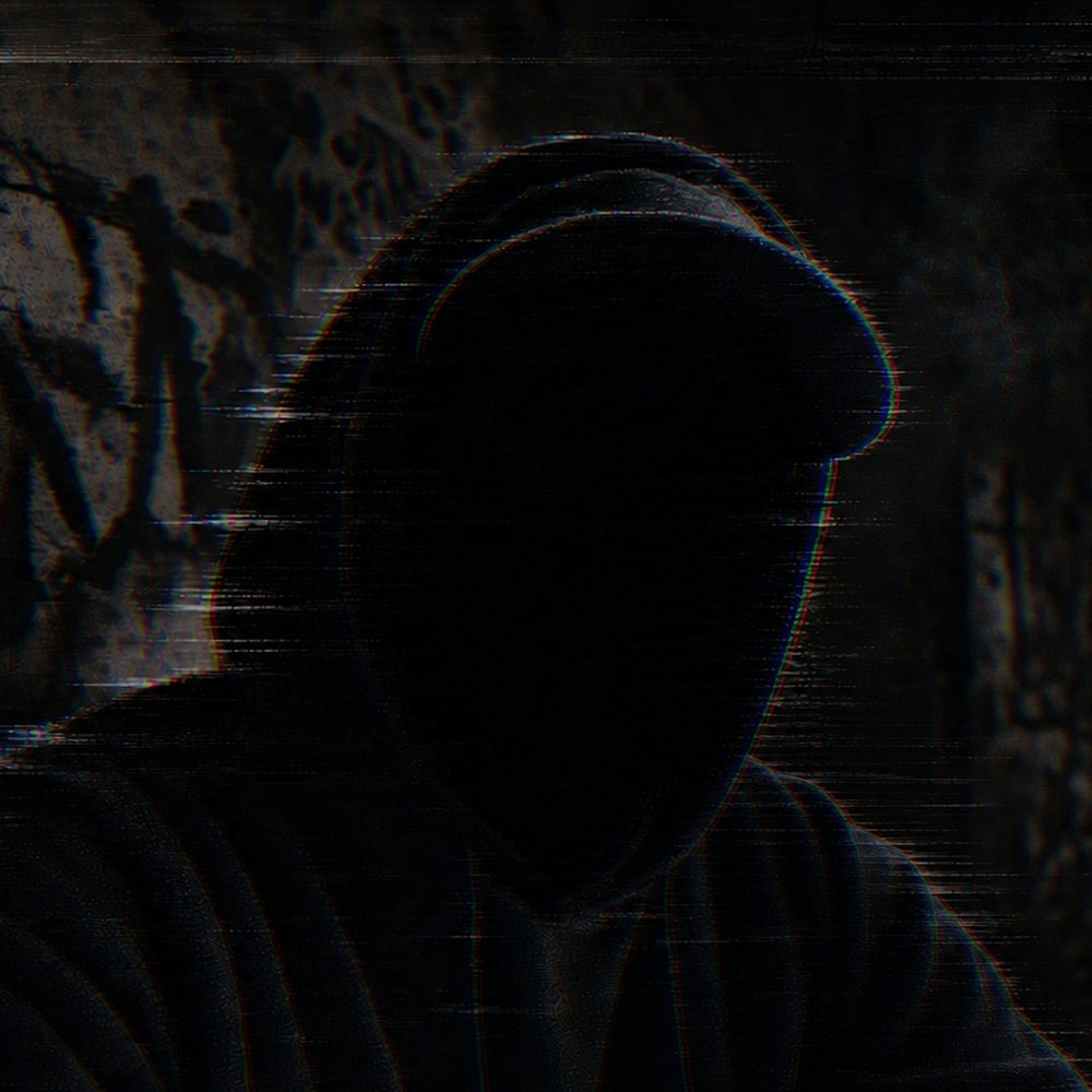 A hooded figure in the dark, face lost in shadow, against a graffiti-covered wall